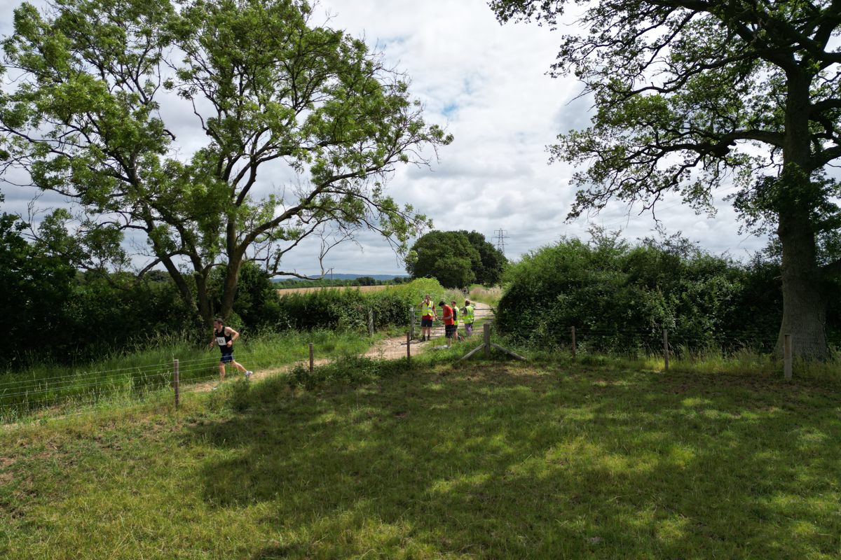 A runner coming through a gate between two oak trees, marshals in hi-vis behind