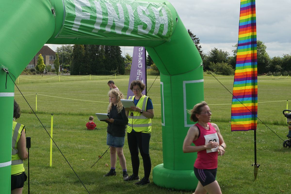 A runner in a pink vest passing the timekeepers at the finish